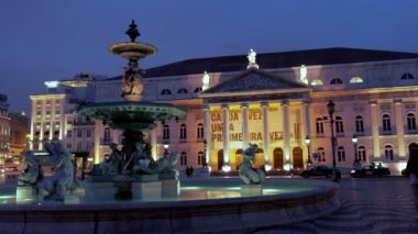 Lizbon Rossio Meydanı'nda arka planda Ulusal Tiyatro ile Aydınlatılmış çeşme karşısında Pan, Portekiz. Akşam saatlerinde çekilen