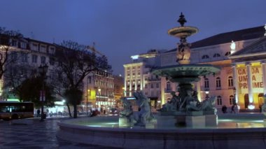 Lizbon Rossio Meydanı'nda ışıklı çeşme ve Ulusal Tiyatro karşısında soldan sağa Pan. Akşamın mavi saatinde çekilmiş