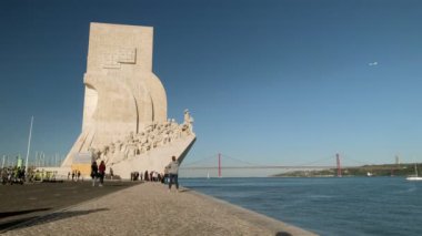 Belem bölgesindeki Tagus nehrinin nehir kıyısında bulunan Keşifler Anıtı 'nın geniş bir klibi. 25 Nisan Köprüsü Lizbon, Portekiz 'de arka planda.