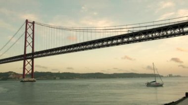 25 Nisan Tagus Köprüsü 'nün alçak açılı klibi. Gün batımında Santo Amaro marinasına dönen küçük bir yat.. 