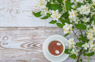 Beyaz renkli ahşap arka planda yasemin çiçekli beyaz bir fincan çay ve dal.