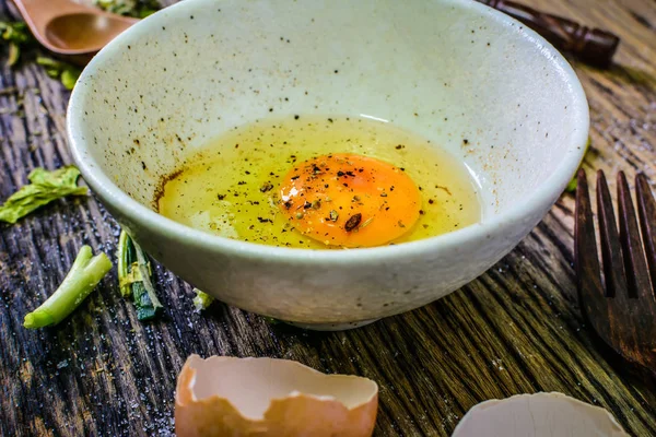 Ahşap bir masa üzerinde bir kapta çiğ yumurta. Yumurta çok pişirmek için kullanılabilir.