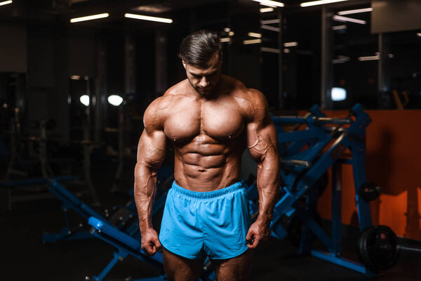 Handsome young fit muscular caucasian man of model appearance workout training in the gym gaining weight pumping up muscle, poses, drinks water  fitness and bodybuilding sport nutrition concept