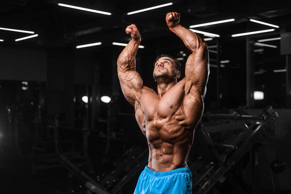 Handsome young fit muscular caucasian man of model appearance workout training in the gym gaining weight pumping up muscle, poses, drinks water  fitness and bodybuilding sport nutrition concept