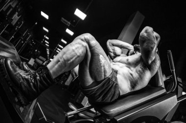 Beyaz kas yakışıklı modeli görünüm egzersiz jimnastik salonu Eğitim kuadriseps bacaklar ve makineleri ve pompalama bir halter ile hamstrings ve fitness vücut geliştirme ve spor beslenme pozlar