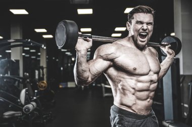 Beyaz kas yakışıklı modeli görünüm egzersiz jimnastik salonu Eğitim kuadriseps bacaklar ve makineleri ve pompalama bir halter ile hamstrings ve fitness vücut geliştirme ve spor beslenme pozlar