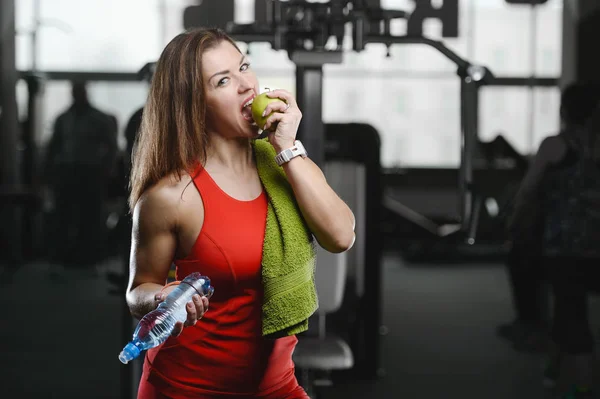 美しい強いセクシーな運動若い白人少女水のボトルとアップル トレーニング トレーニング ダイエット腹筋の筋肉をポンピングとボディービル健康管理とフィットネスの概念をポーズでジムで — ストック写真