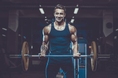 Yakışıklı, formda, kaslı, beyaz bir adam spor salonunda antrenman yapıyor. Kilo alıyor, kaslarını şişiriyor, fitness ve vücut geliştirme sporları yapıyor.