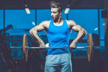 Yakışıklı, formda, kaslı, beyaz bir adam spor salonunda antrenman yapıyor. Kilo alıyor, kaslarını şişiriyor, fitness ve vücut geliştirme sporları yapıyor.