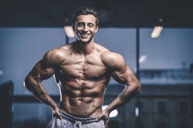 Yakışıklı, formda, kaslı, beyaz bir adam spor salonunda antrenman yapıyor. Kilo alıyor, kaslarını şişiriyor, fitness ve vücut geliştirme sporları yapıyor.