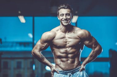 Yakışıklı, formda, kaslı, beyaz bir adam spor salonunda antrenman yapıyor. Kilo alıyor, kaslarını şişiriyor, fitness ve vücut geliştirme sporları yapıyor.