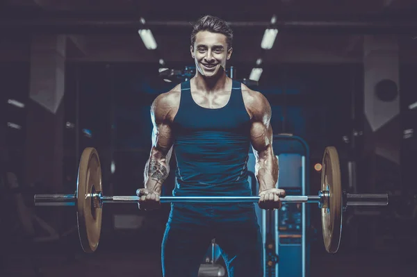 Handsome young fit muscular caucasian man of model appearance workout training in the gym gaining weight pumping up muscles and poses fitness and bodybuilding sport concept