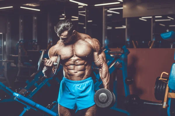 Handsome young fit muscular caucasian man of model appearance workout training in the gym gaining weight pumping up muscle, poses, drinks water  fitness and bodybuilding sport nutrition concept