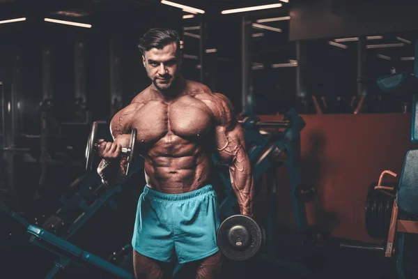 Handsome young fit muscular caucasian man of model appearance workout training in the gym gaining weight pumping up muscle, poses, drinks water  fitness and bodybuilding sport nutrition concept