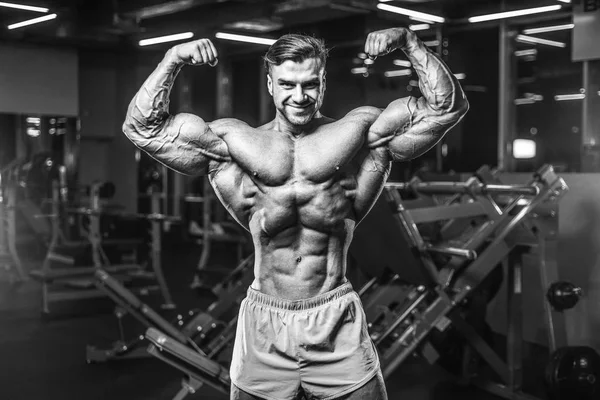 Handsome young fit muscular caucasian man of model appearance workout training in the gym gaining weight pumping up muscle, poses, drinks water  fitness and bodybuilding sport nutrition concept