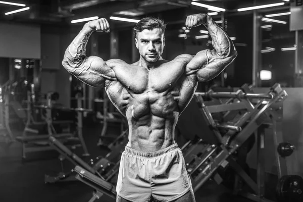 Handsome young fit muscular caucasian man of model appearance workout training in the gym gaining weight pumping up muscle, poses, drinks water  fitness and bodybuilding sport nutrition concept