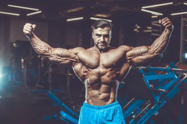 Handsome young fit muscular caucasian man of model appearance workout training in the gym gaining weight pumping up muscle, poses, drinks water  fitness and bodybuilding sport nutrition concept