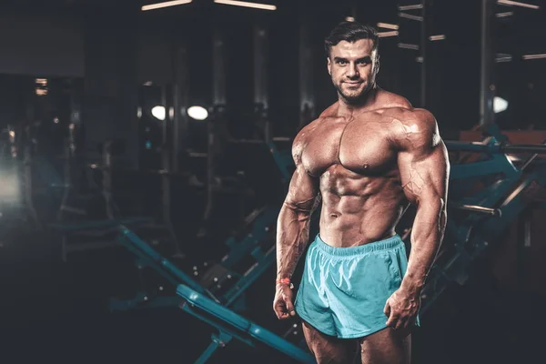 Handsome young fit muscular caucasian man of model appearance workout training in the gym gaining weight pumping up muscle, poses, drinks water  fitness and bodybuilding sport nutrition concept