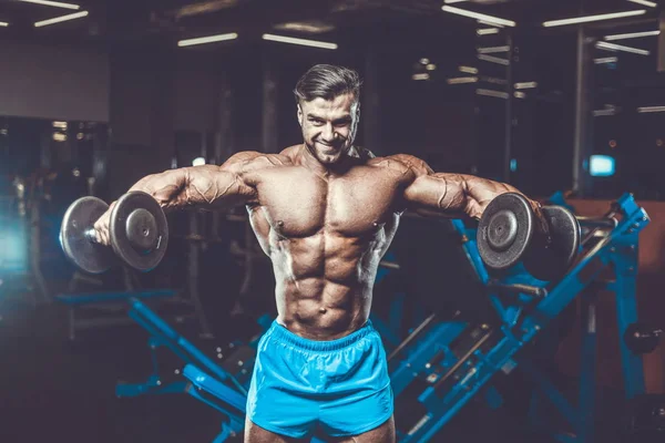 Handsome young fit muscular caucasian man of model appearance workout training in the gym gaining weight pumping up muscle, poses, drinks water  fitness and bodybuilding sport nutrition concept