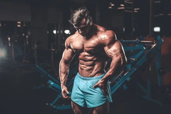 Handsome young fit muscular caucasian man of model appearance workout training in the gym gaining weight pumping up muscle, poses, drinks water  fitness and bodybuilding sport nutrition concept