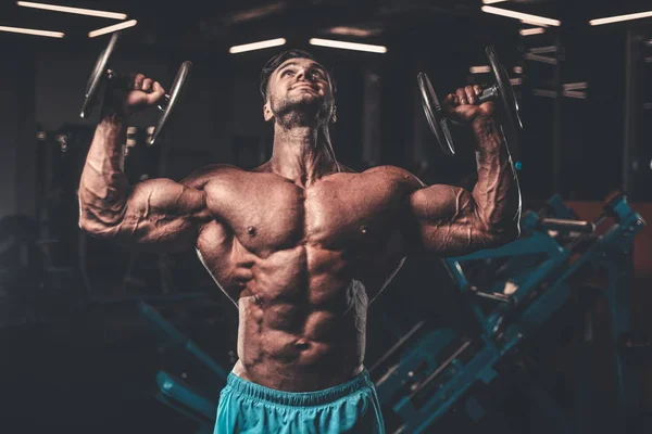 Handsome young fit muscular caucasian man of model appearance workout training in the gym gaining weight pumping up muscle, poses, drinks water  fitness and bodybuilding sport nutrition concept