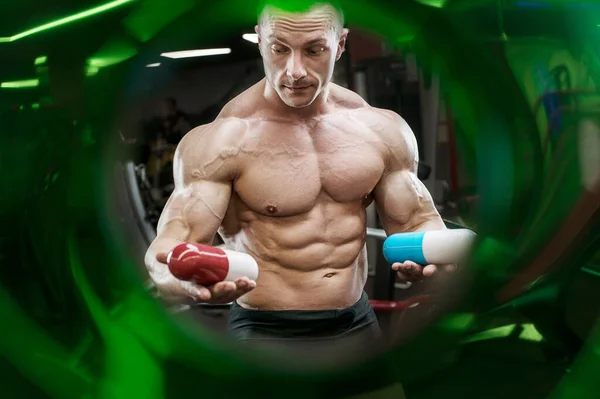 Fitness man at workout in gym with protein powder jar. Bodybuilding and healthy lifestyle concept background. Muscular bodybuilder with sport nutrition supplements jar in gym naked torso