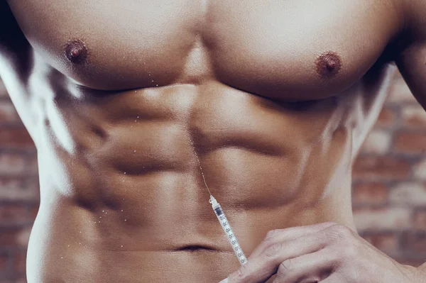 Bodybuilder doing steroid syringe injection in gym. Strong athletic rough muscular man pumping up abs muscles workout fitness and bodybuilding healthy concept design. abdominal exercises naked torso