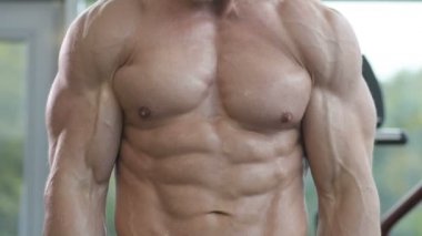 Beyaz tenli atletik adam kaslarını şişiriyor. Güçlü vücut geliştirici, karın kasları, trisepsleri, göğsü ve omuzları var. Fitness ve vücut geliştirme konsepti