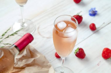 Bir kadeh pembe şarap, beyaz ahşap masanın üzerinde rustik tahtaüzerine şişe. Şarap tadımı konsepti 