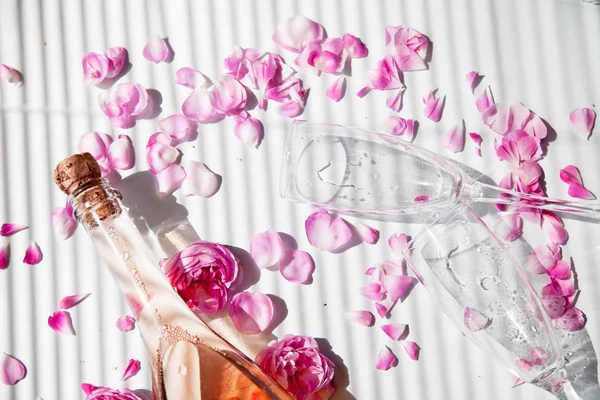 A bottle of pink sparkling wine and glasses with rose petals on a white background. Wine tasting concept