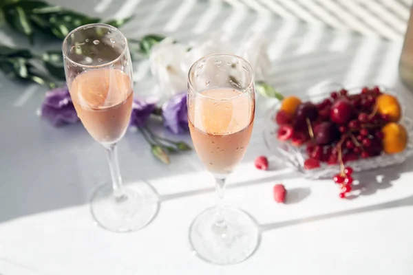 Copas de vino rosa en la mesa junto a flores y frutas —  Fotos de Stock