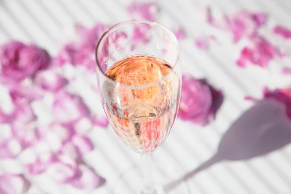 A glass of cold champagne and rose petals on a white background, — Stock Photo, Image