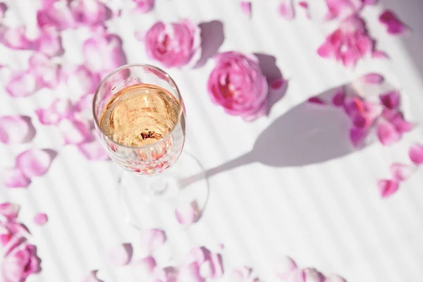 Una copa de champán y pétalos de rosa sobre un fondo blanco de las mujeres —  Fotos de Stock