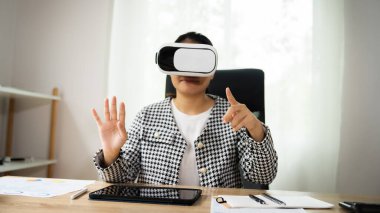 Siyah beyaz kareli ceket giyen bir kadın sanal gerçeklik kulaklığıyla video oyunu oynuyor.