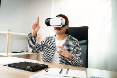 Siyah beyaz ceket giyen bir kadın bir kalemle bir video oyunu oynuyor. Parmağıyla ekranı işaret ediyor.