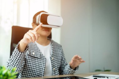 Siyah beyaz ceket giyen bir kadın sanal gerçeklik kulaklığıyla bir video oyunu oynuyor. Ekrandaki bir şeyi işaret ediyor.