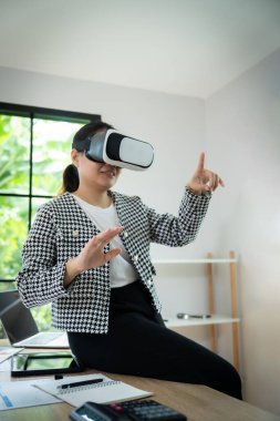 Siyah beyaz ceket giyen bir kadın sanal gerçeklik kulaklığıyla bir video oyunu oynuyor. Gülümsüyor ve kameraya el sallıyor.