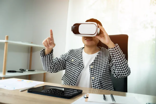 Siyah beyaz kareli ceket giyen bir kadın sanal gerçeklik kulaklığıyla video oyunu oynuyor.