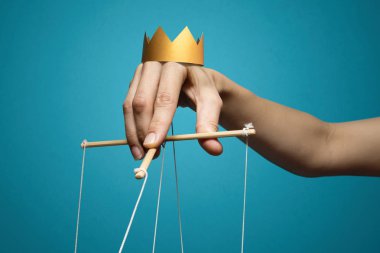 Concept of manipulation. Hand with crown holds strings for manipulation on blue background. clipart