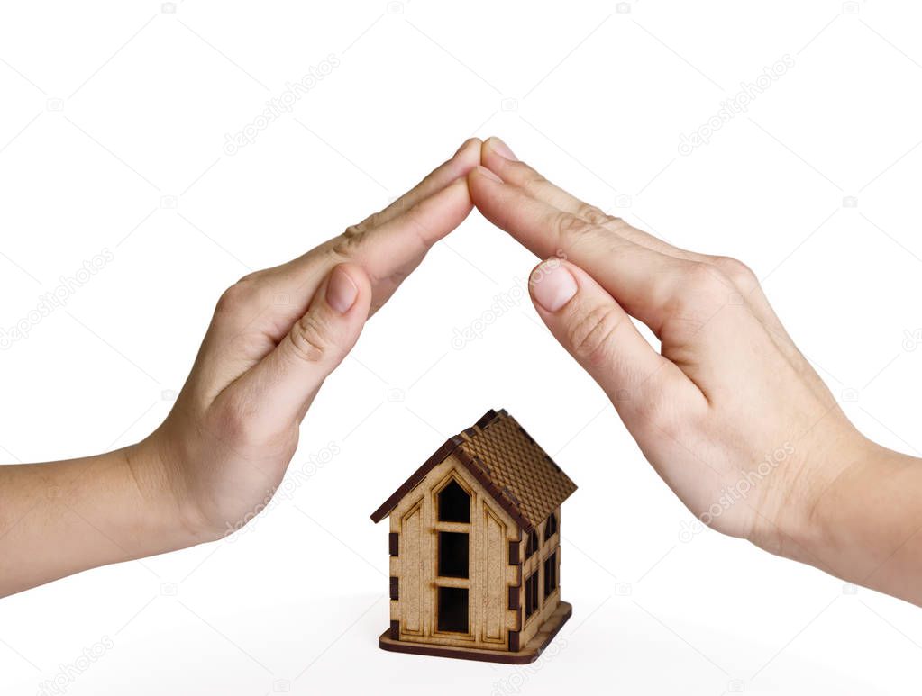 Two palms over wooden model house on white isolated background. Concept of insuranse real estate, security and safety house.