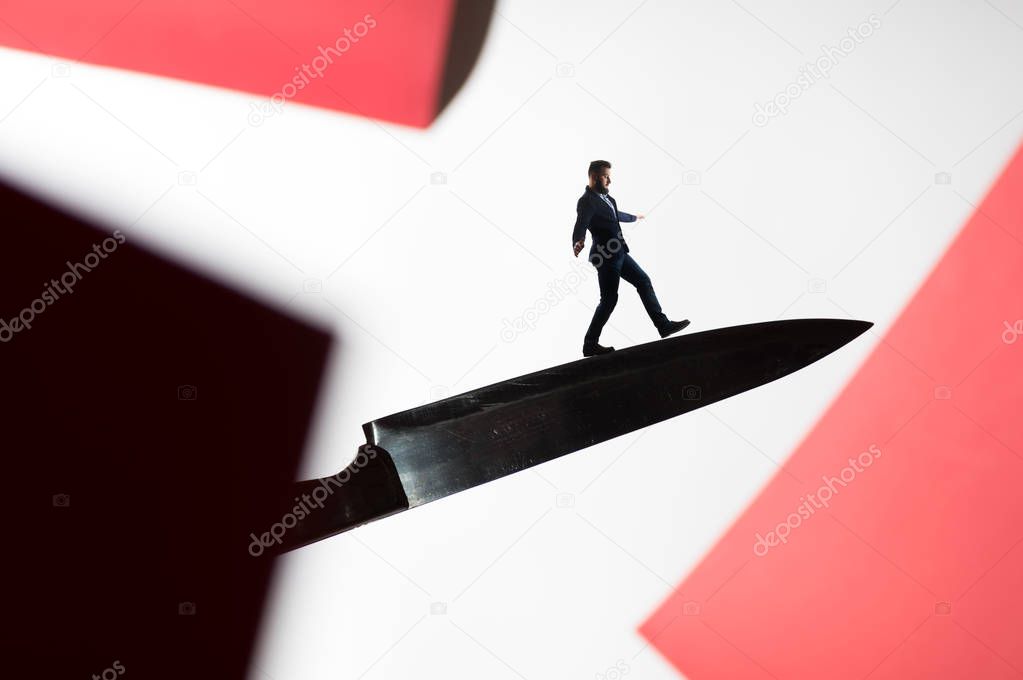 The concept of risk. A man in a business suit walks on the blade of the knife. Image.