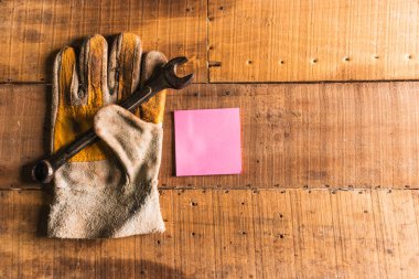 Deri eldiven, üzerinde bir yüz çizilmiş, kırsal ahşap çalışma masasının üzerinde paslı bir İngiliz anahtarı tutuyor.
