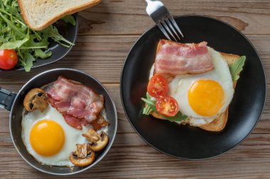 Siyah tabak ve çatal, mantar ve rukkola ile tavada kızarmış yumurta üst görünümü