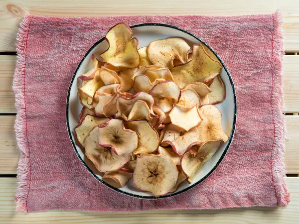 Vista superior de chips de manzana en un plato rústico sobre una toalla roja iluminada por la luz del sol . — Foto de Stock