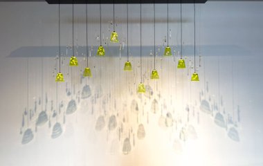 Sarı ve berrak cam parçalarıyla asılı bir lamba. Ampul tavandan sarkıyor ve bir ışık kaynağı tarafından aydınlatılıyor.