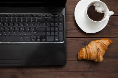 Dizüstü yakınındaki taze kruvasan ve kahve fincan üstten görünüm