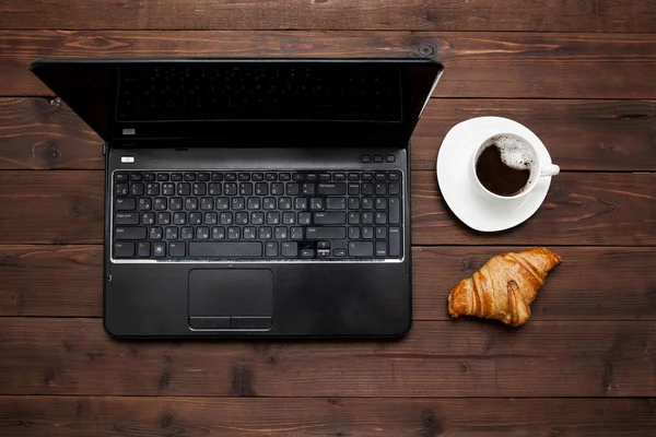 Dizüstü yakınındaki taze kruvasan ve kahve fincan üstten görünüm