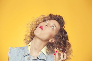 çikolatalı çörek ısırma ve üzerinde izole sarı arka plan arıyorum kız