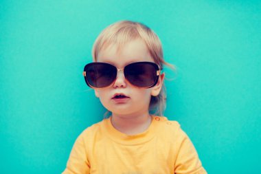 çok güzel bebek kız güneş gözlüğü ve mavi izole sarı tişört ayakta
