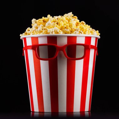 Siyah arka planda izole patlamış mısır ve gözlük ile kağıt çizgili kova